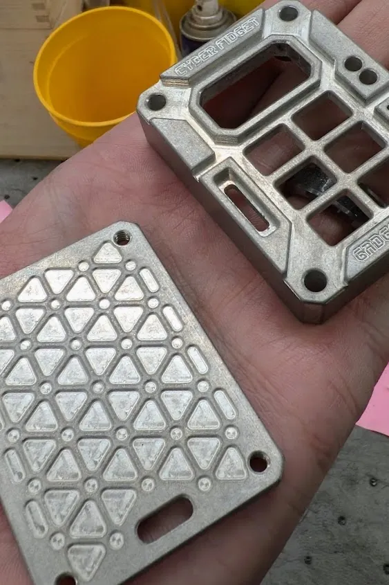 An empty aluminum case front and a backplate with a triangle pattern machined into it, held in an open hand
