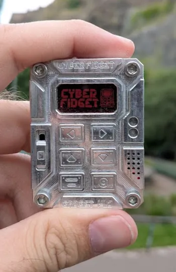 A Cyber Fidget held between finger and thumb, its screen glowing red with the Cyber Fidget logo